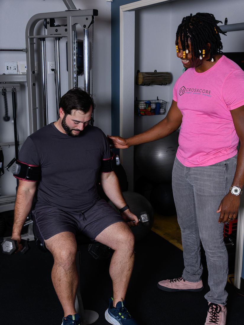 Brandon coaching a client through seated dumbbell work with blood flow restriction cuffs